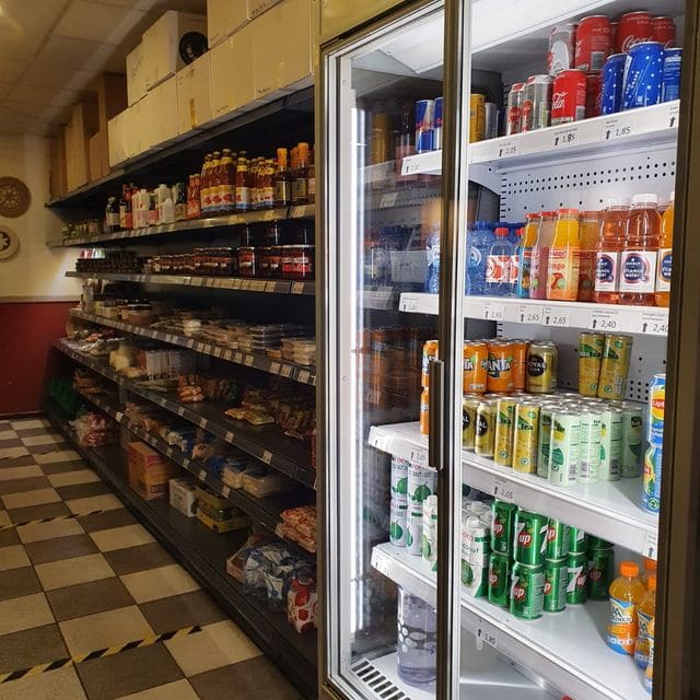 Schappen met Indonesische sauzen, pakjes en koelkasten vol drinken in de toko